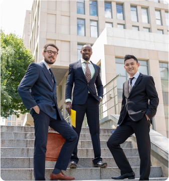 Three individuals in business attire standing confidently on outdoor steps of a building
